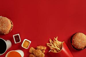 Two hamburgers and french fries, sauces and drinks on red background. Fast food. Top view, flat lay with copyspace photo