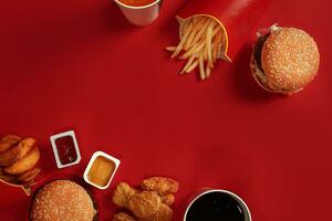 Two hamburgers and french fries, sauces and drinks on red background. Fast food. Top view, flat lay with copyspace photo