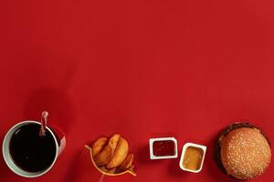 Concept of mock up burger, potatoes, sauce and drink on red background. Copy space for text and logo. photo