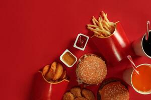 Two hamburgers and french fries, sauces and drinks on red background. Fast food. Top view, flat lay with copyspace photo