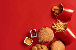 Fast food dish top view. Meat burger, potato chips and nuggets on red background. Takeaway composition. photo