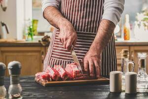 Man cuts of fresh piece of meat on a wooden cutting board in the home kitchen photo