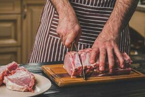 Man cuts of fresh piece of meat on a wooden cutting board in the home kitchen photo