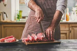 Man cuts of fresh piece of beef on a wooden cutting board in the home kitchen photo