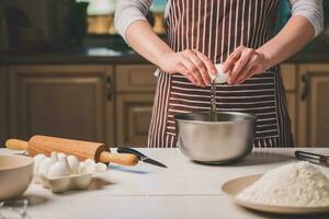 Young woman breaking egg over bowl with dough, close-up photo