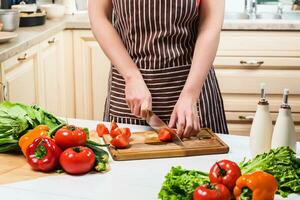 Young woman cooking in the kitchen at home. A woman cuts a tomato and vegetables with a knife. photo