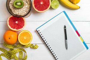 Healthy breakfast with oatmeal, fresh fruits and notebook on rustic wooden table. photo