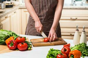 Young woman cooking in the kitchen at home. A woman cuts a tomato and vegetables with a knife. photo