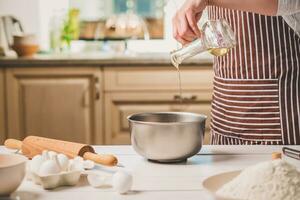 Young woman pouring oil into a bowl with dough, close-up photo