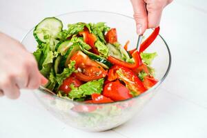 Young woman dressing vegetable salad with olive oil on a white background photo