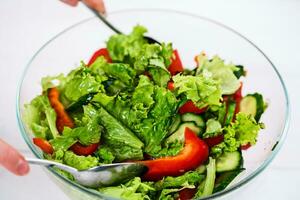 Young woman dressing vegetable salad with olive oil on a white background photo