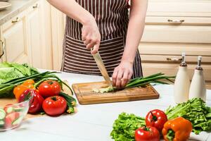 Young woman cooking in the kitchen at home. A woman cuts a green onion and vegetables with a knife. photo