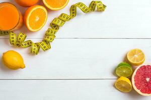 Fresh fruits with tape measure over white wooden background. Top view photo