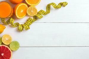 Fresh fruits with tape measure over white wooden background. Top view photo