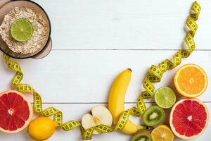 Fresh fruits with tape measure over white wooden background. Top view photo