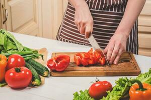 Young woman cooking in the kitchen at home. A woman cuts a pepper and vegetables with a knife. photo