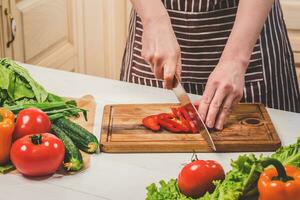 Young woman cooking in the kitchen at home. A woman cuts a pepper and vegetables with a knife. photo