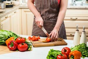 Young woman cooking in the kitchen at home. A woman cuts a tomato and vegetables with a knife. photo