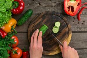 Female hands cutting cucumber at table, top view photo