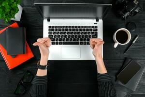 Woman working at the office table. Top view of human hands, laptop keyboard, a cup of coffee, smartphone, notebook and a flower on a wooden table background photo