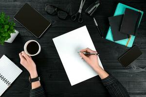 Businesswoman desk with with different objects. A woman's hand writes in a notebook photo