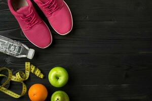 Athlete's set with female clothing, sneakers and bottle of water on dark background photo