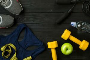 Athlete's set with female clothing, sneakers and bottle of water on dark background photo