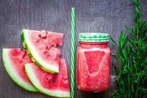 Watermelon smoothie and slices on dark wooden background. Flat lay or top view. photo