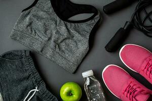 Athlete's set with female clothing, sneakers and bottle of water on gray background photo
