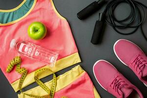 Athlete's set with female clothing, sneakers and bottle of water on gray background photo