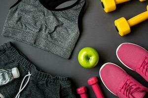 Athlete's set with female clothing, sneakers and bottle of water on gray background photo