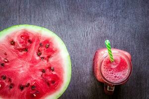 Watermelon smoothie and a half of fresh watermelon on dark wooden background. Flat lay or top view. photo