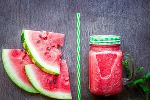 Watermelon smoothie and slices on dark wooden background. Flat lay or top view. photo