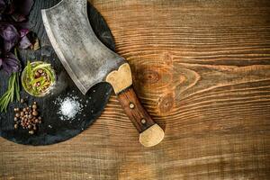 Basil and a sprig of rosemary with ax for meat on wooden background. Top view photo