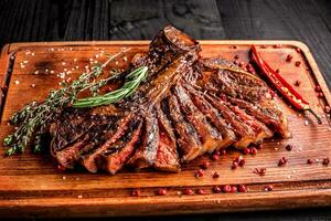 Sliced medium rare grilled steak on rustic cutting board with rosemary and spices , dark rustic wooden background, top view photo