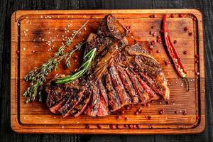 Sliced medium rare grilled steak on rustic cutting board with rosemary and spices , dark rustic wooden background, top view photo