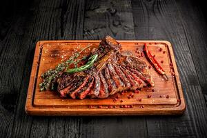Sliced medium rare grilled steak on rustic cutting board with rosemary and spices , dark rustic wooden background, top view photo