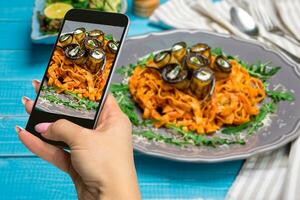 Photographing food concept - woman takes picture of pasta with eggplants, tomato, cheese, arugula and salad photo