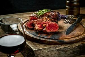 Grilled ribeye beef steak with red wine, herbs and spices on wooden table photo