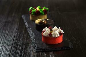 Side view on mini party tartlets with fresh fruit, chocolate, nuts and cream on black slate background photo