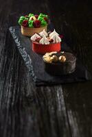 Side view on mini party tartlets with fresh fruit, chocolate, nuts and cream on black slate background photo