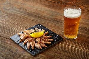 Grilled shrimps on black board pan and beer on wooden table photo