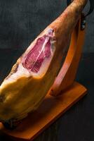 Whole mediterranean traditional jamon on a wooden stand with a knife lean on a table. Dark image photo