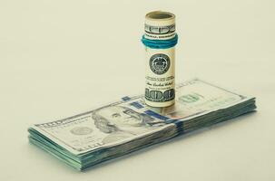 A coiled 100 dollar bill which rests on another angled 100 dollar bill isolated on white background photo