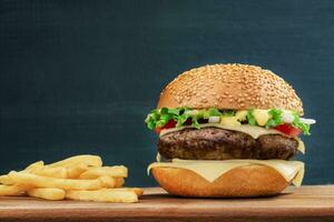 Fast food. Cheeseburger and french fries on a wooden board, on dark background photo