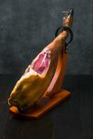 Whole mediterranean traditional jamon on a wooden stand with a knife lean on a table. Dark image photo