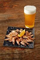 Grilled shrimps on black board pan and beer on wooden table photo