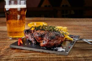 Beer being poured into glass with gourmet steak and french fries on wooden background. photo