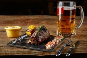 Grilled tenderloin Steak roastbeef and mushrooms sauce on black cutting board and glass of beer on wooden table photo