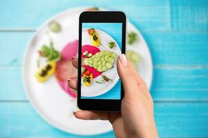 Woman hands taking photo fish with mixed vegetable with smartphone.